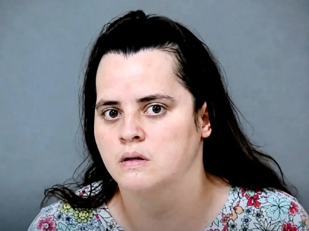 Booking photo of Shelbey Fernandez, a woman with long dark hair pulled partly back, wearing a floral top, photographed against a gray wall.